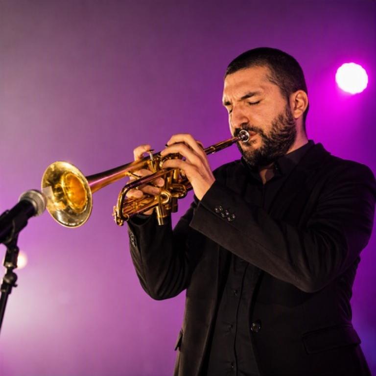 Ibrahim Maalouf performing with his signature trumpet on stage, illuminated by vibrant purple and gold concert lighting.